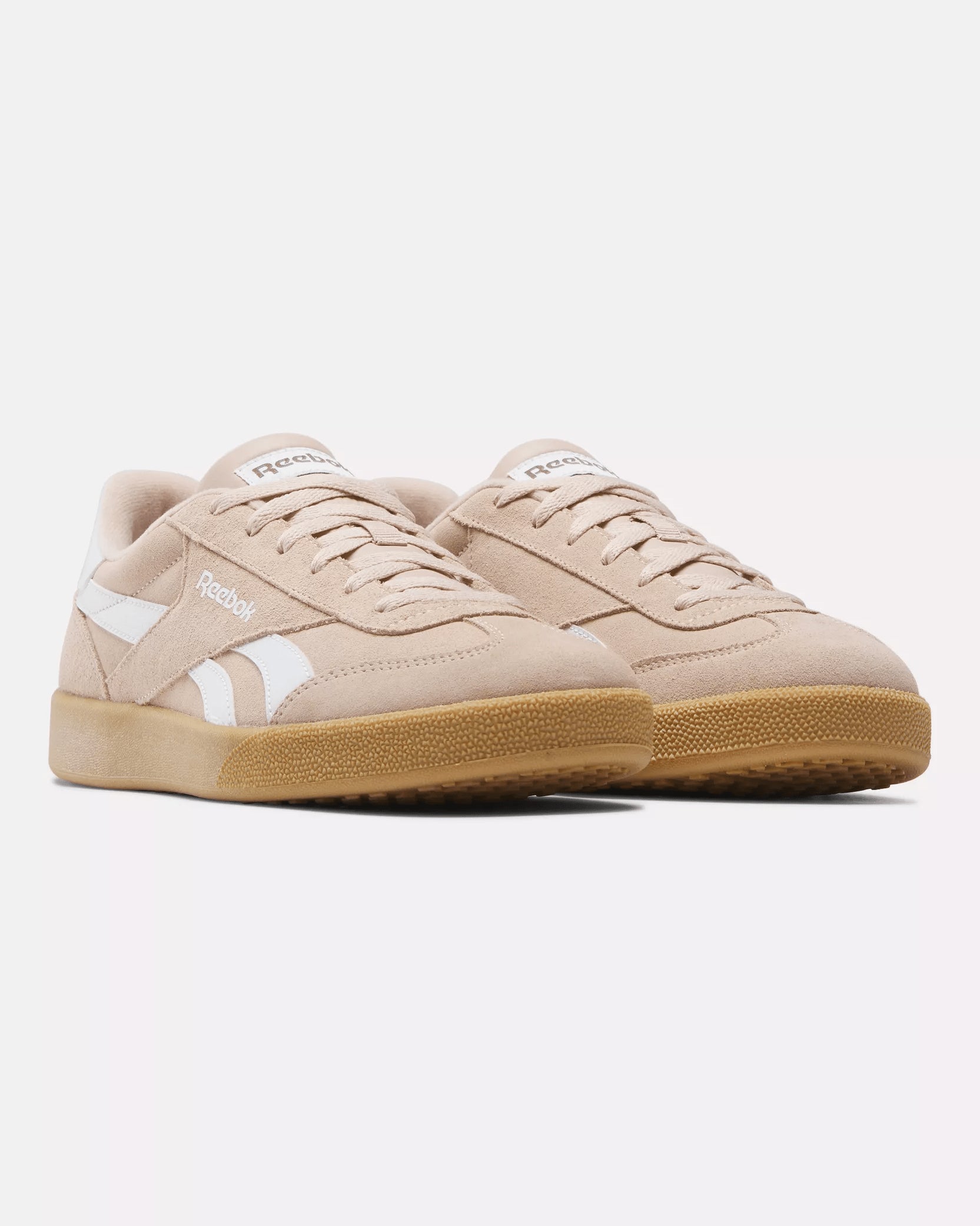 Side view of beige pink Reebok sneakers with white logo details and gum outsole, featuring a classic retro-inspired design.