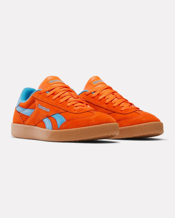 A pair of orange low-top Reebok sneakers with blue accents, orange laces, and gum rubber soles, shown from a front-side angle.