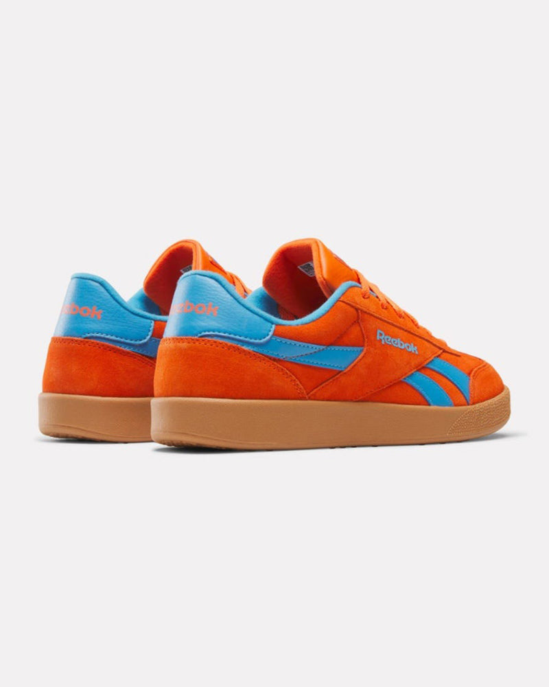 A pair of orange Reebok sneakers with blue accents, gum soles, and branding on the sides and heels, shown from a rear-side angle.