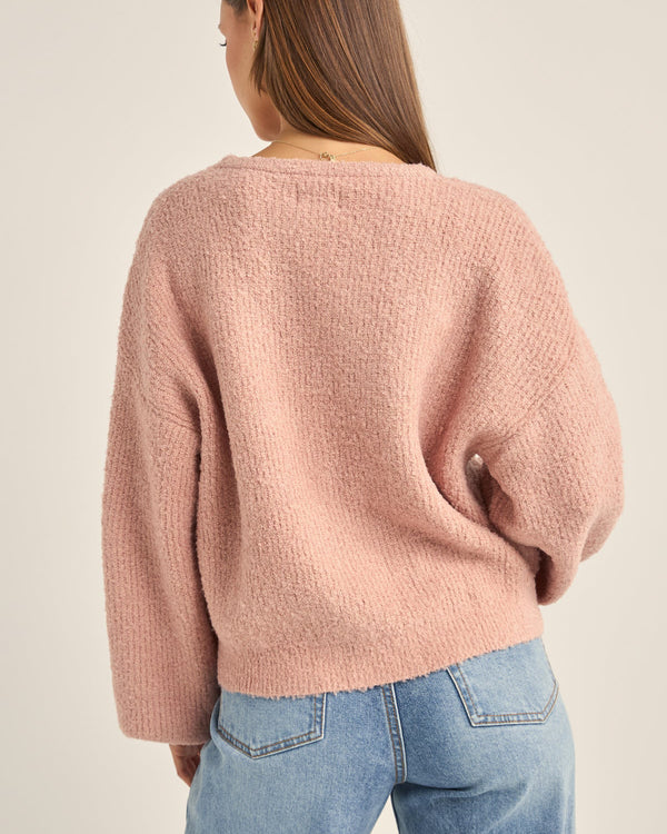 Back view of a woman wearing a soft pink oversized knit sweater with a textured finish, dropped shoulders, and relaxed fit.