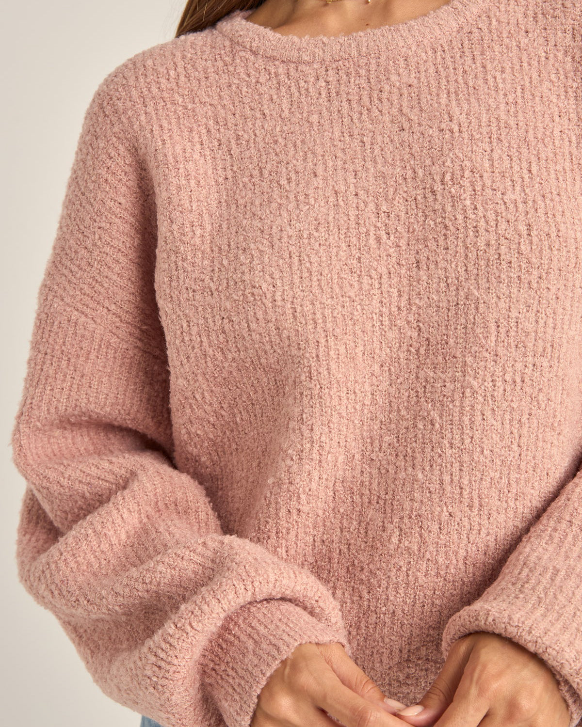 Close-up of a soft pink textured sweater with a relaxed fit and balloon sleeves, worn by a model with hands visible."