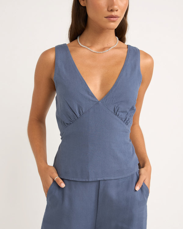 Close-up of a sleeveless blue V-neck top with ruched detailing at the bust, paired with matching high-waisted pants.