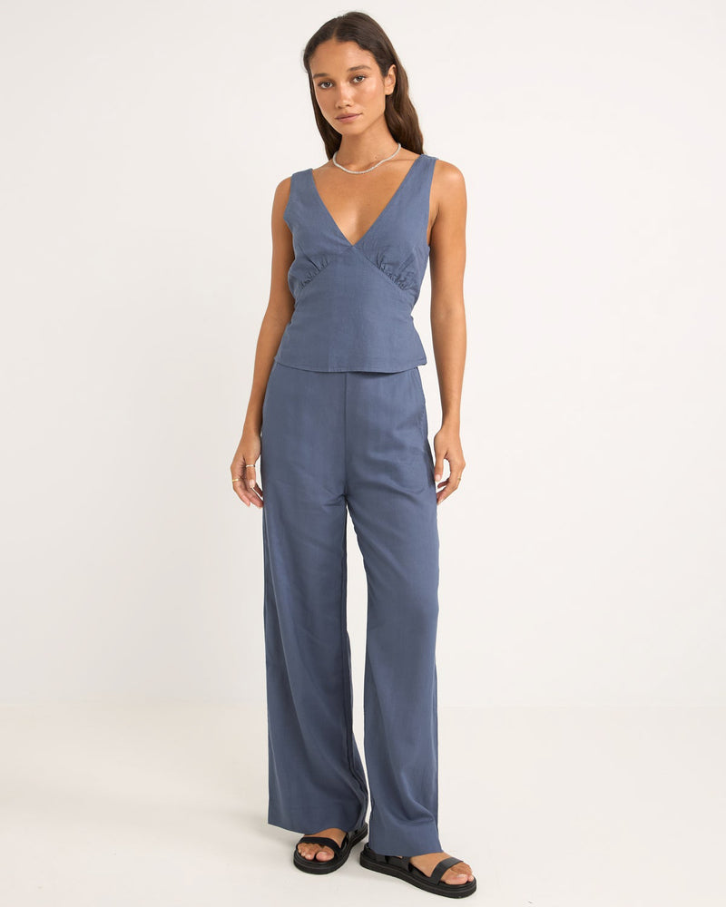 Sleeveless blue top with a deep V-neckline, fitted waist, and subtle ruching detail, paired with matching wide-leg pants.