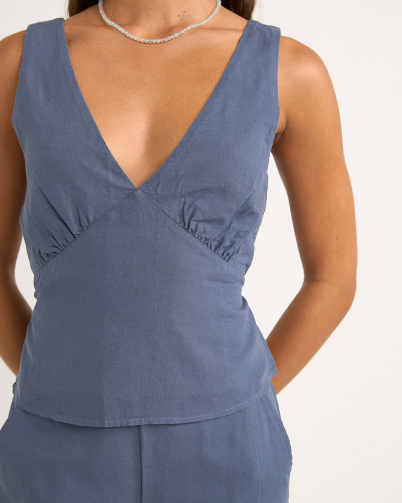 Close-up of a blue sleeveless V-neck top with subtle ruching at the bust and a fitted waist, paired with matching pants.