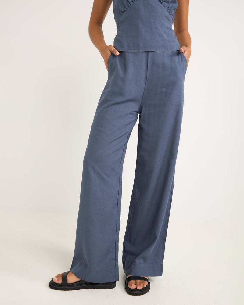 Women's wide-leg blue pants with a high waist, side pockets, and a relaxed fit, styled with black sandals.