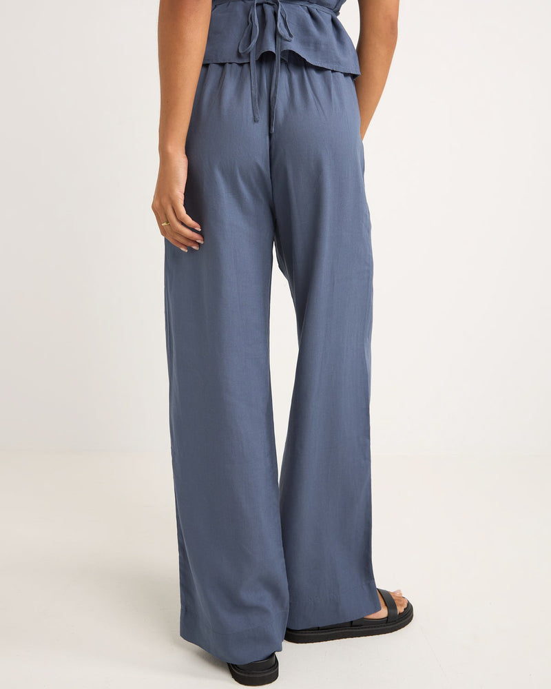 Back view of women's wide-leg blue pants with a relaxed fit, elastic waistband, and flowy fabric, styled with sandals.