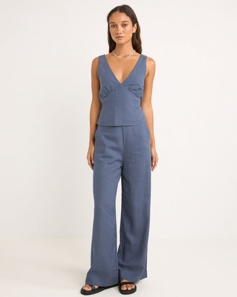 Woman wearing high-waisted, wide-leg blue pants with a relaxed fit, paired with a matching V-neck top and black sandals.