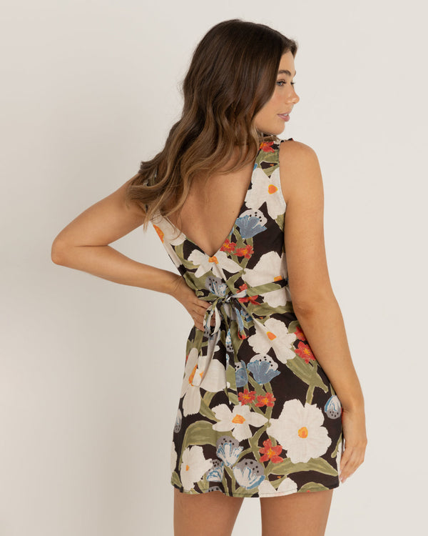 A model wearing a floral dress with a V-back and tie detail, featuring a mix of large flowers in vibrant colors.