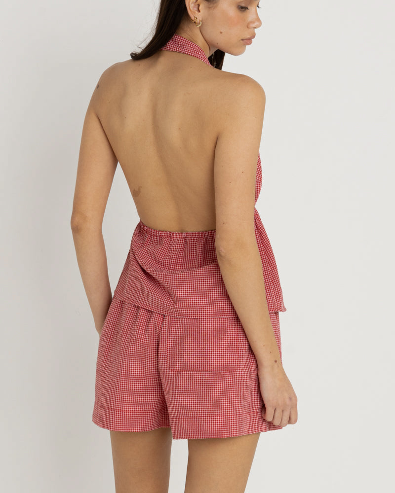 Back view of red gingham shorts with a loose fit, elastic waistband, paired with an open-back halter top.