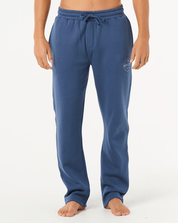 Man wearing blue Rip Curl sweatpants with a drawstring waist and small logo on the left thigh, standing barefoot.