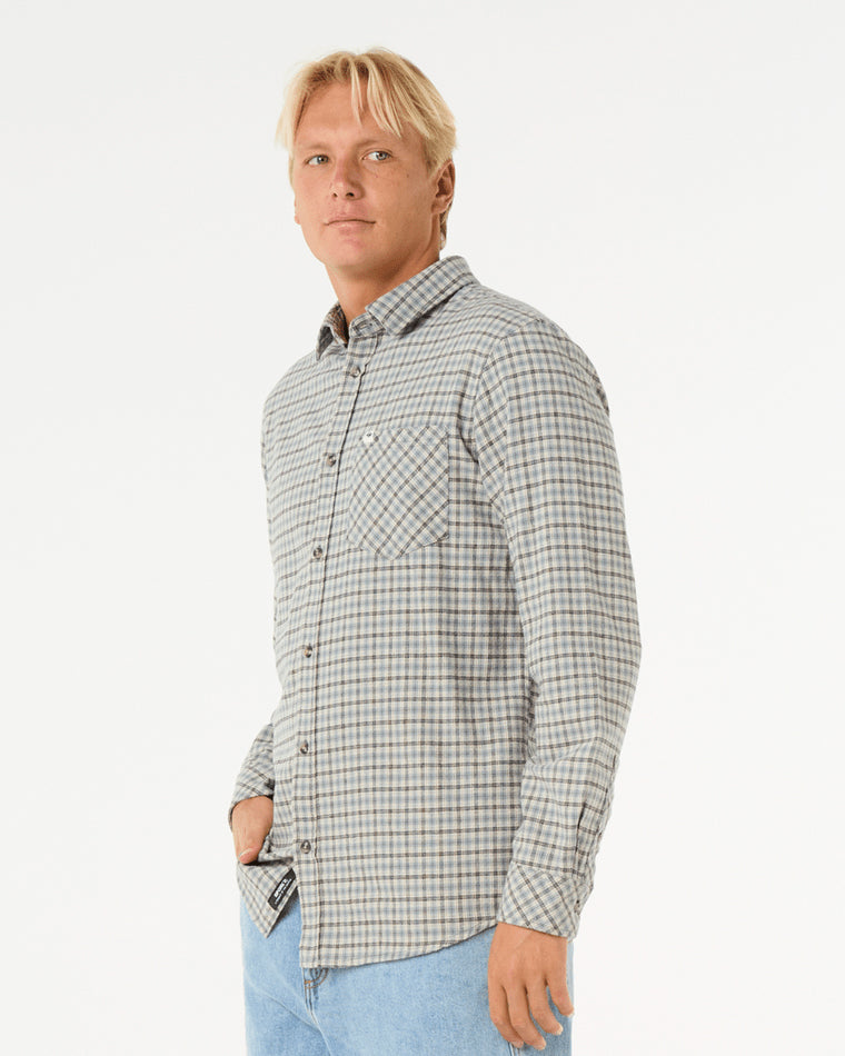 Side view of a man wearing a long-sleeve plaid button-up shirt with a chest pocket, paired with light blue denim jeans.