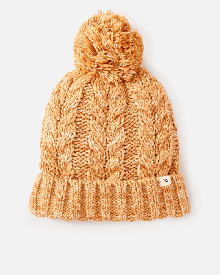 Chunky knit beanie in a warm caramel hue with a cable knit pattern, pom-pom on top, and a small Rip Curl logo tag on the cuff.