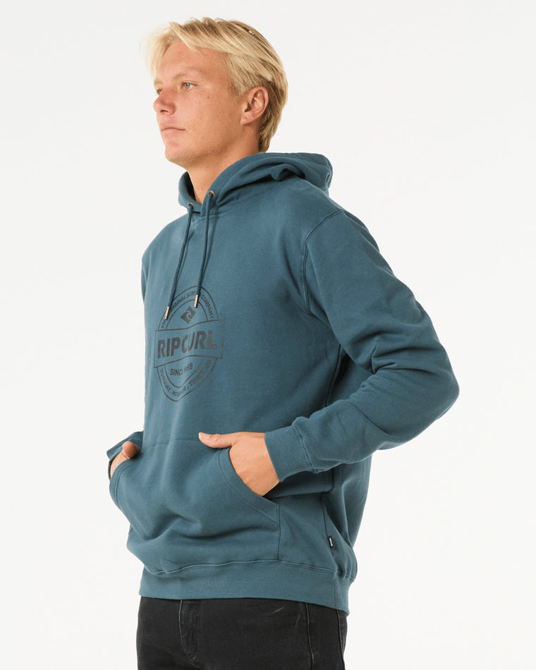 Side view of a man wearing a teal Rip Curl hoodie with a front logo, drawstring hood, and kangaroo pocket.