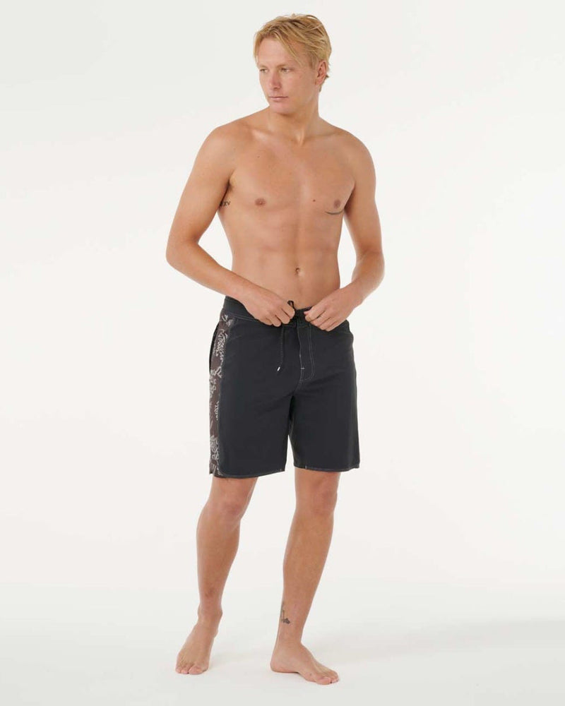 Full body shot of black printed boardshorts styled for surf or swim, worn with no shirt.