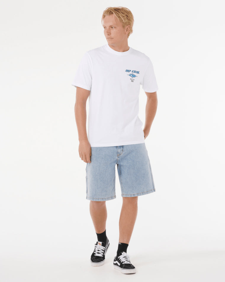 Model wearing a white Rip Curl t-shirt with a small chest logo, paired with light blue denim shorts and black sneakers.