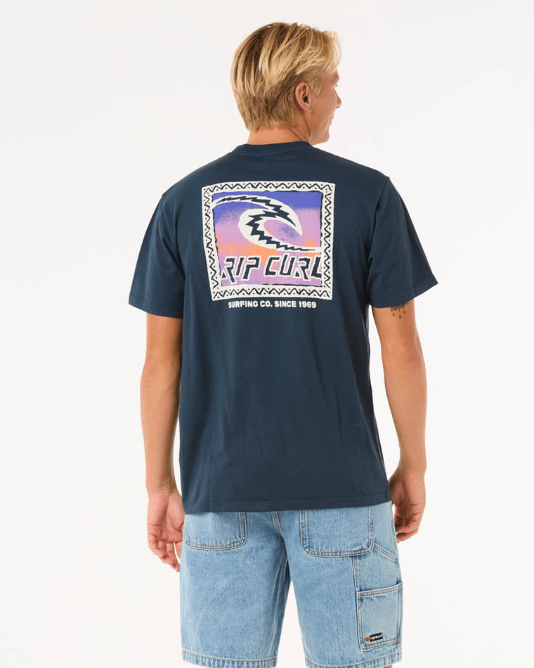 A navy blue t-shirt featuring a bold back graphic with Rip Curl branding, vibrant colors, and text, paired with denim shorts.