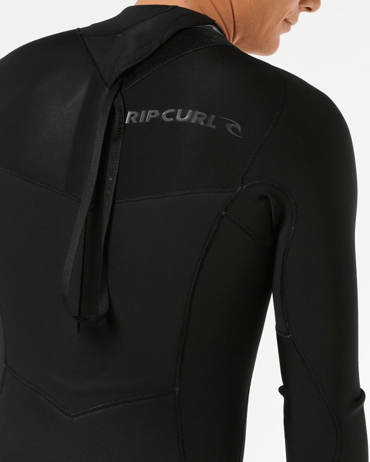 Close-up of the back of a black Rip Curl wetsuit, featuring a back zip entry with a pull strap and logo detailing.