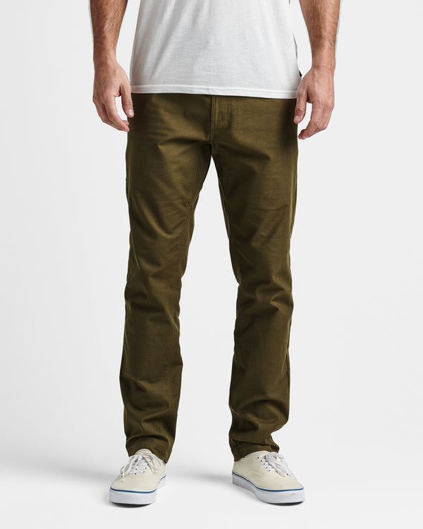 Model wearing olive green slim-fit pants with a white t-shirt and off-white sneakers against a plain background.