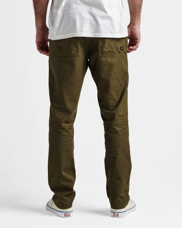 Back view of model wearing olive green slim-fit pants with patch pockets, white t-shirt, and off-white sneakers.