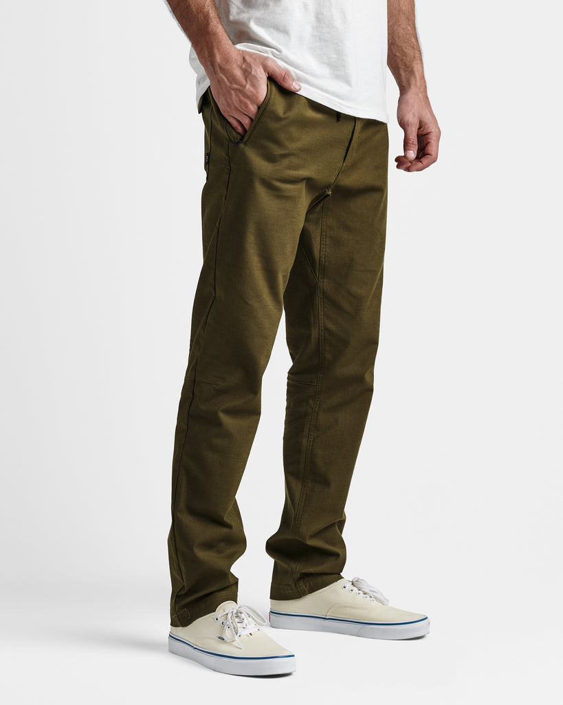 Side view of model wearing olive green slim-fit pants with front pockets, white t-shirt, and off-white sneakers.