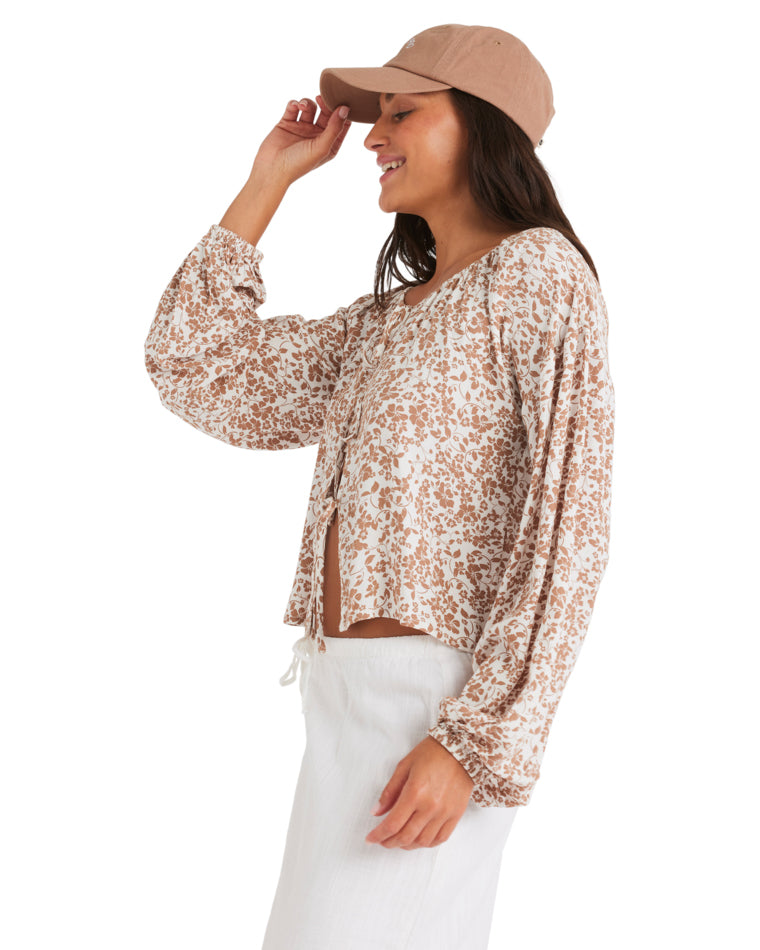 Side view of woman in floral long-sleeve blouse and white skirt, touching her cap.