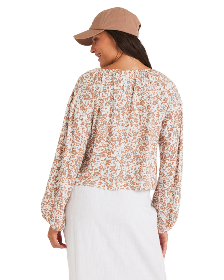 Woman wearing a long-sleeve floral tie-front blouse and white midi skirt, seen from the back.