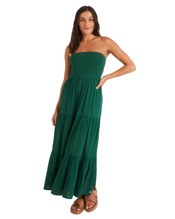 Woman wearing a strapless green tiered maxi dress with smocked bodice, standing with one hand in pocket.