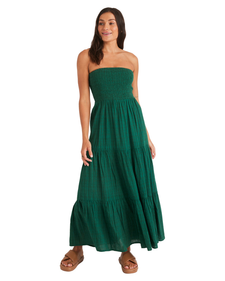 Woman standing in a green strapless maxi dress with tiered layers, hands relaxed and wearing tan sandals.