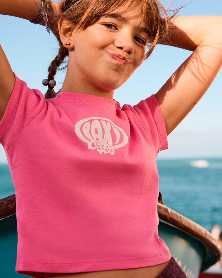 Girl wearing a pink Roxy tee with retro logo and floral detail on the chest.