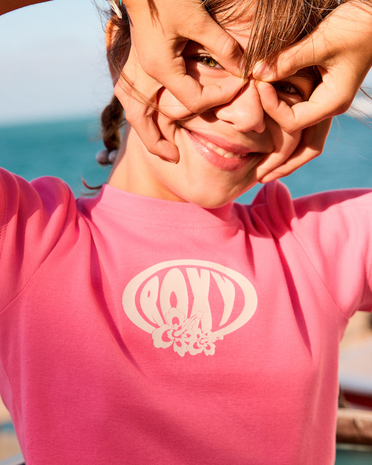 Close-up of girl smiling in a pink Roxy tee with bold retro logo and floral detail.