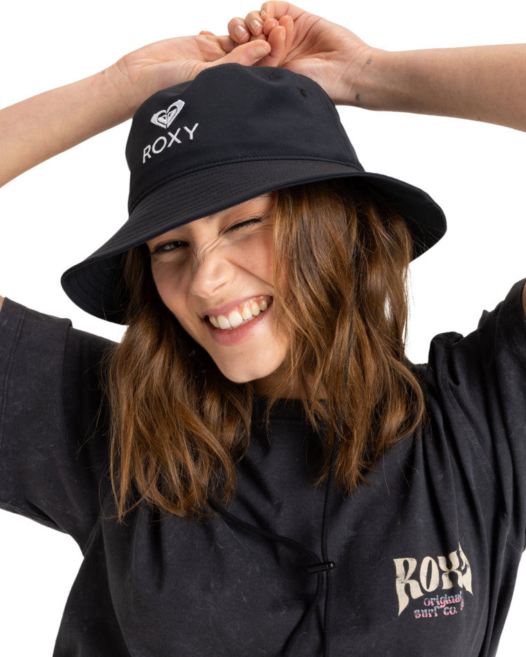 Woman wearing black Roxy bucket hat and smiling with hands raised.