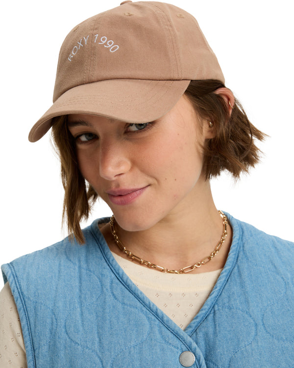 Woman wearing a tan brown cap with “ROXY 1990” embroidered in white on the front.