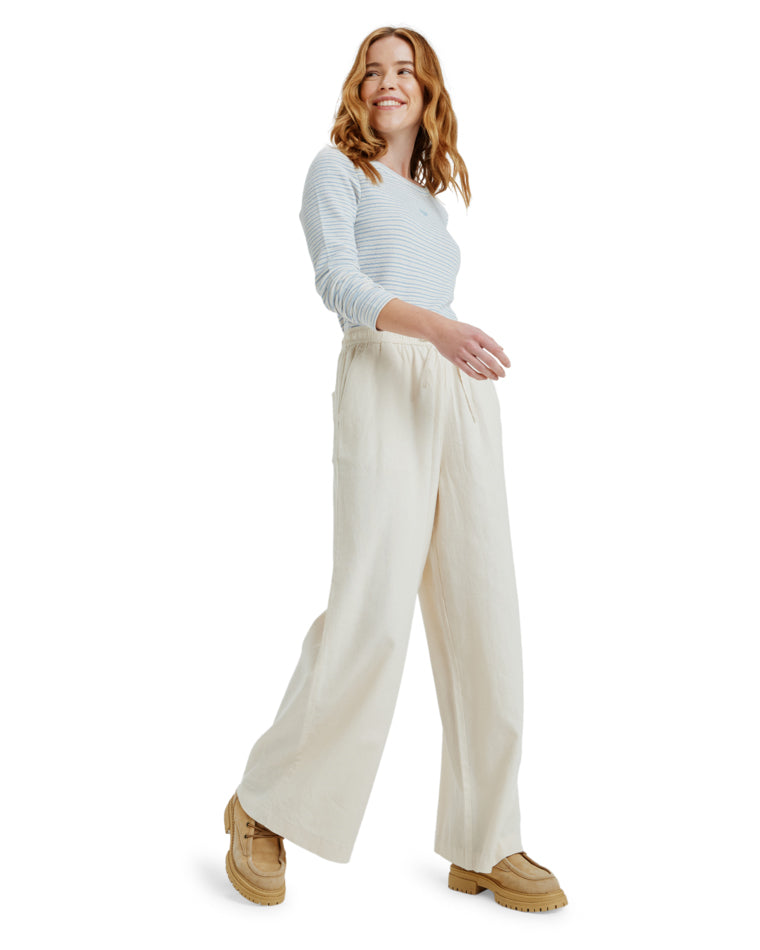 Woman walking in cream wide-leg pants paired with tan boots and striped top.