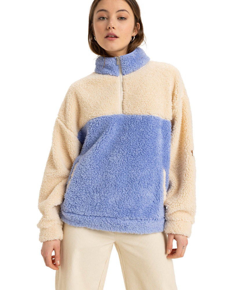 A model wearing a cozy color-block fleece pullover with cream and light blue panels, a half-zip collar, and a relaxed fit.