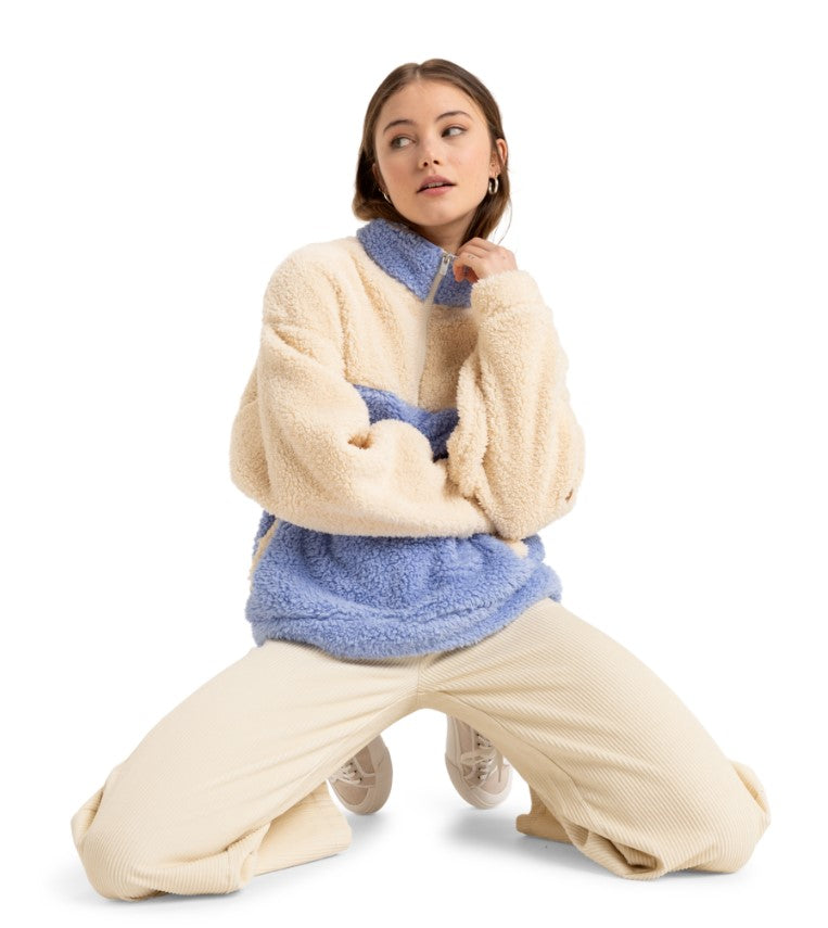 A model wearing a cozy cream and light blue color-block fleece pullover paired with wide-leg cream pants and white sneakers.