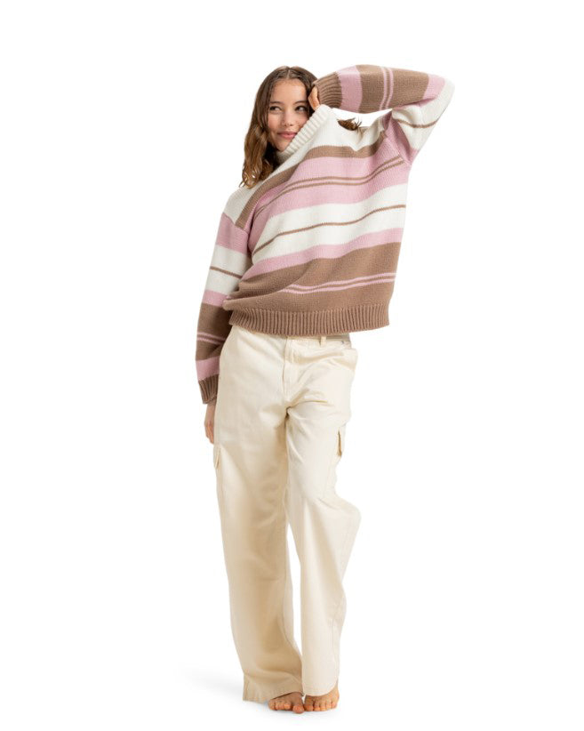 Smiling woman wearing a cozy striped knit sweater in brown, pink, and white, paired with beige cargo pants, barefoot.