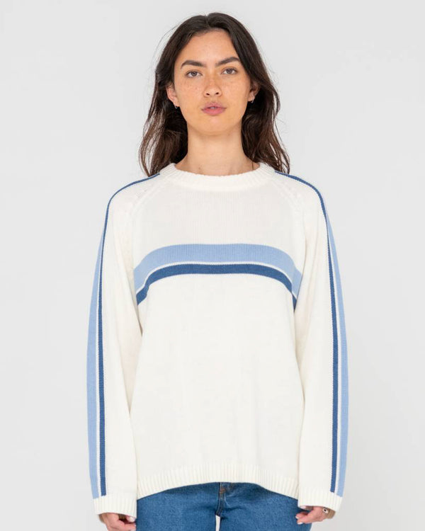 Front view of a woman wearing a cream knit sweater with blue stripe details across the chest and down the sleeves.