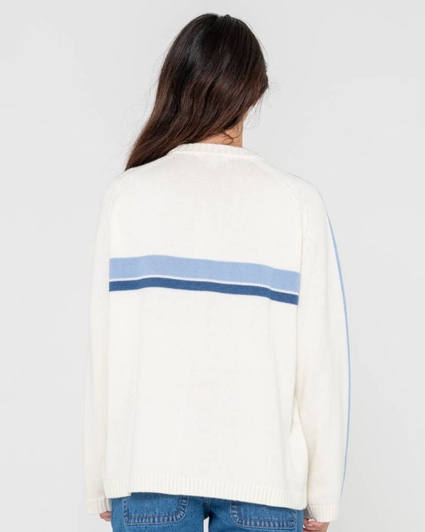 Back view of a woman wearing a cream knit sweater with blue stripe details across the upper back and down the sleeves.