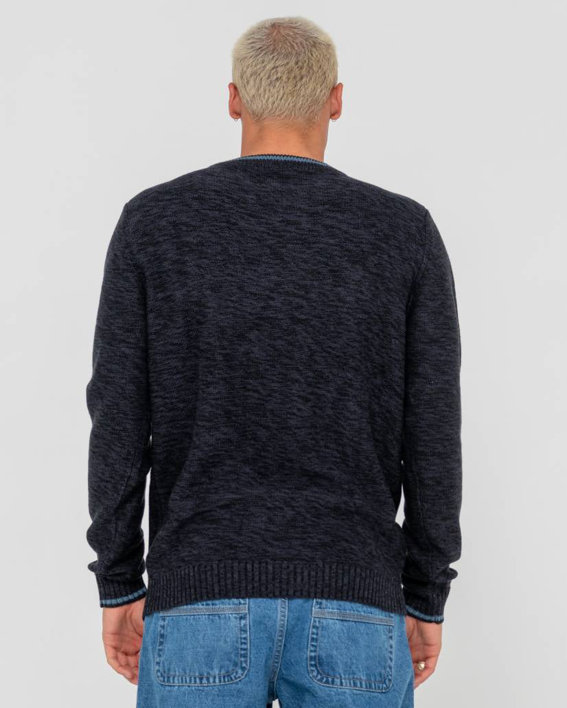 Back view of a male model wearing a dark navy knit sweater with ribbed cuffs and hem, paired with light blue denim jeans.