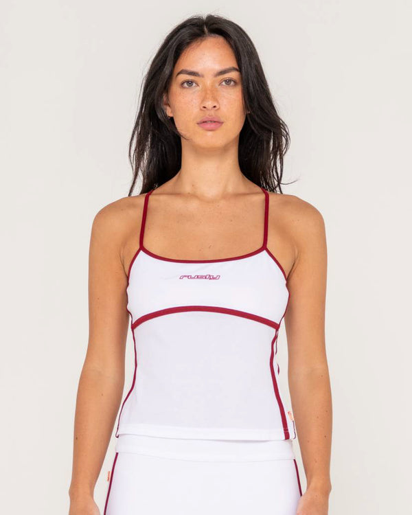 Female model wearing a white fitted tank top with thin straps, red contrast piping, and a small logo on the chest.