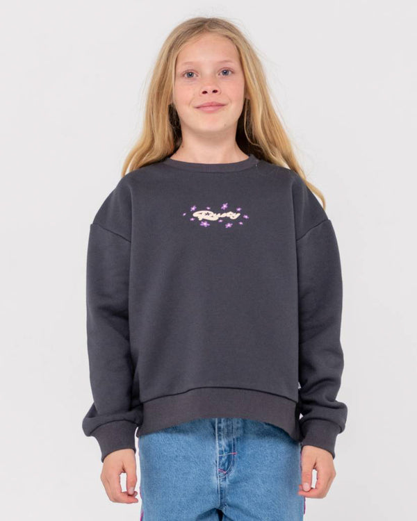 Girl wearing a dark grey oversized sweatshirt with a small printed logo and purple star details, paired with blue jeans.