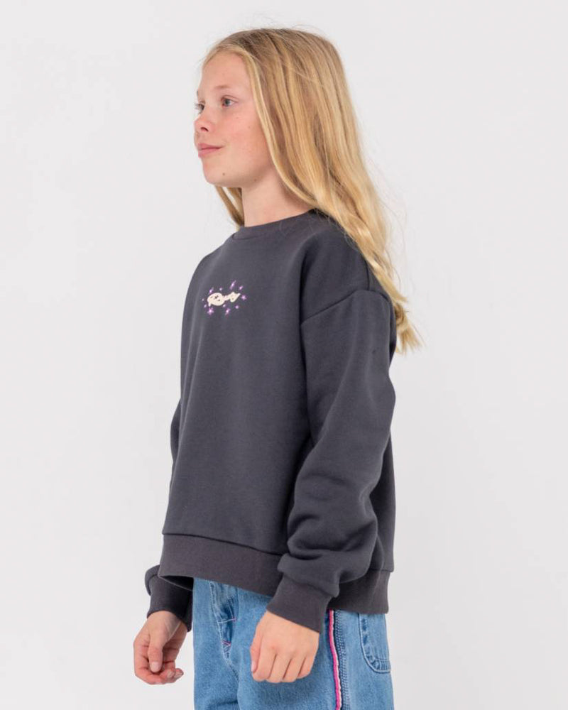 Side view of a girl wearing a dark grey oversized sweatshirt with a small logo design on the chest, paired with blue jeans.