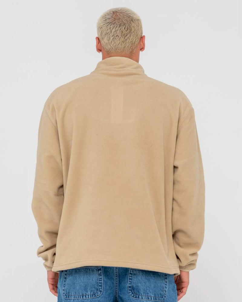 Back view of a man wearing a beige fleece pullover with a high collar, long sleeves, and a relaxed fit, paired with blue jeans.