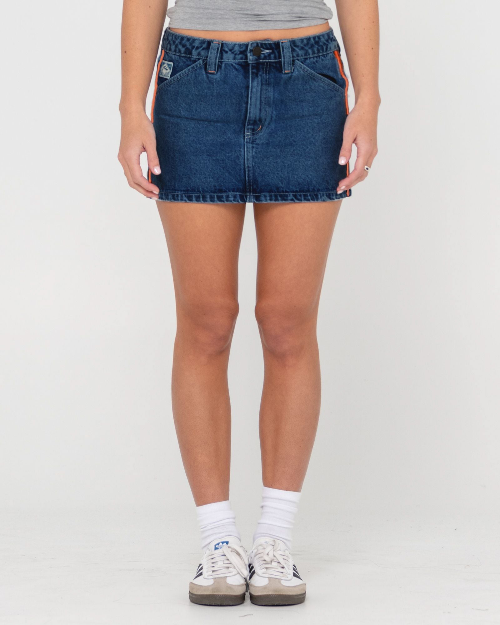 Front view of a denim skirt with a button-up closure, pockets, and an orange accent stripe on the side.