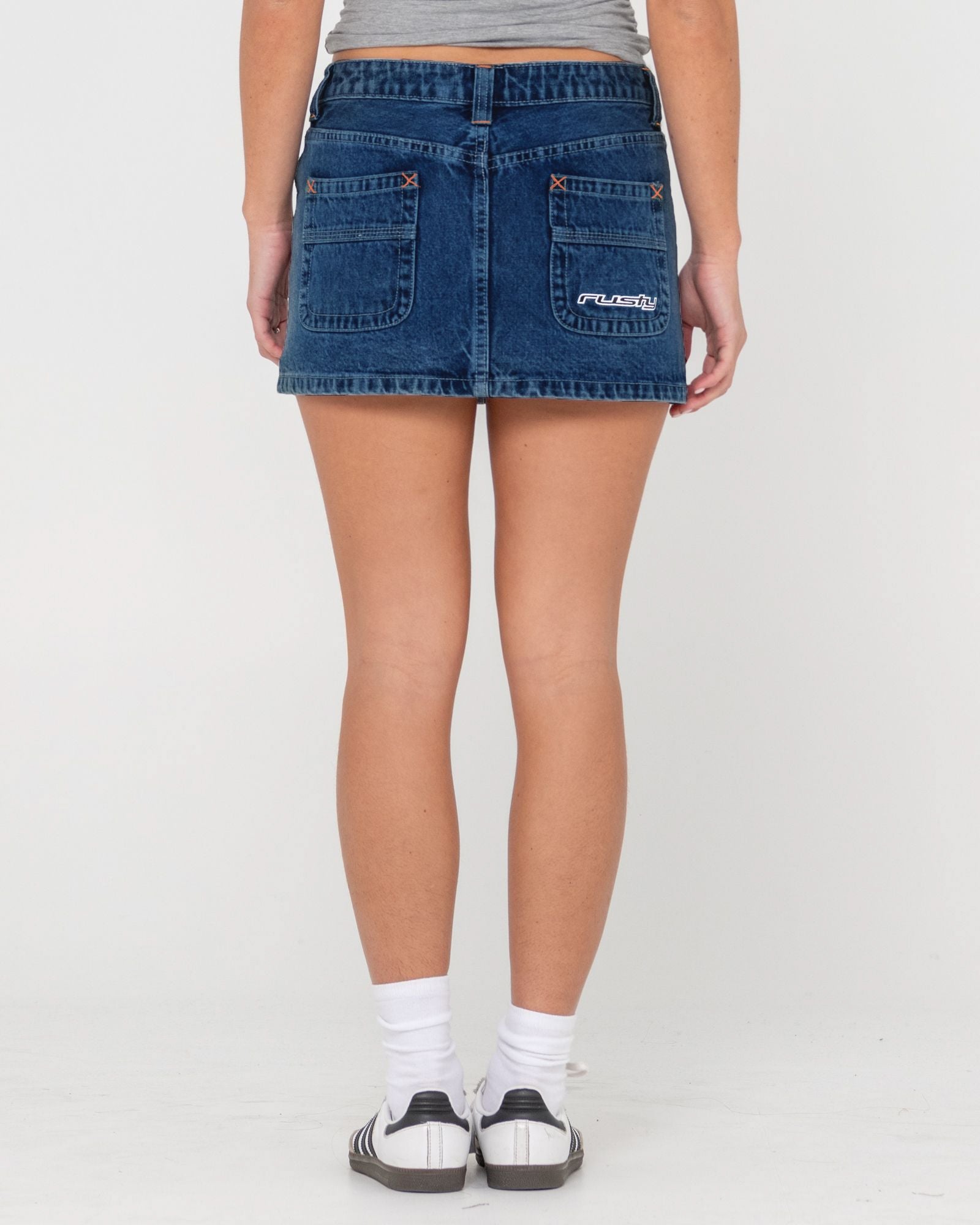 Back view of a denim skirt with back pockets featuring orange stitching and a logo detail.
