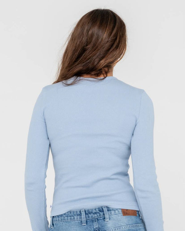 Back view of a woman wearing a light blue long-sleeve ribbed top with a fitted silhouette and classic crew neckline.