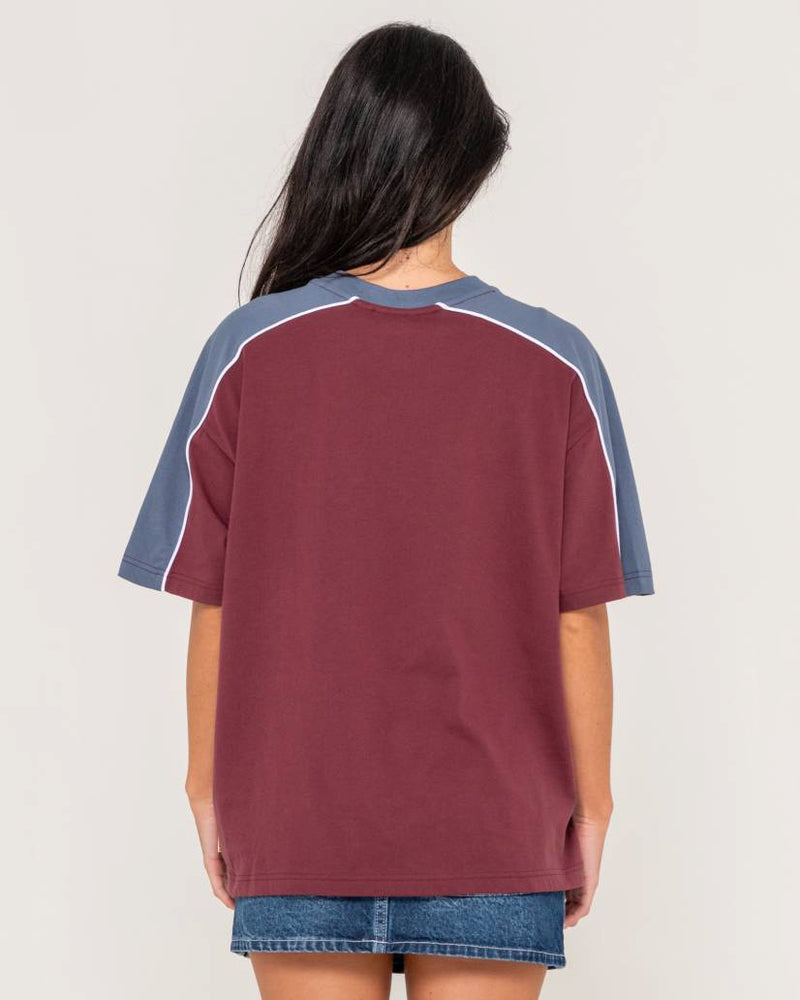 Back view of a Rusty oversized T-shirt in burgundy with navy contrast sleeves and white piping, paired with a denim skirt.