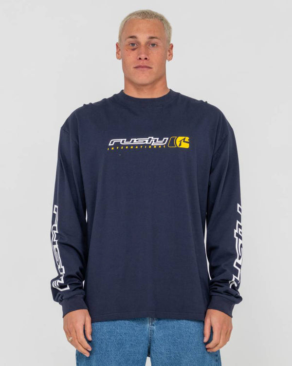 Model wearing a navy blue long-sleeve Rusty shirt with a yellow and white logo on the chest and branding on the sleeves.