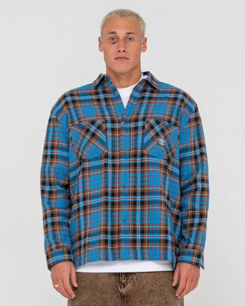 Man wearing a blue and brown plaid button-up flannel shirt with dual chest pockets, layered over a white t-shirt.