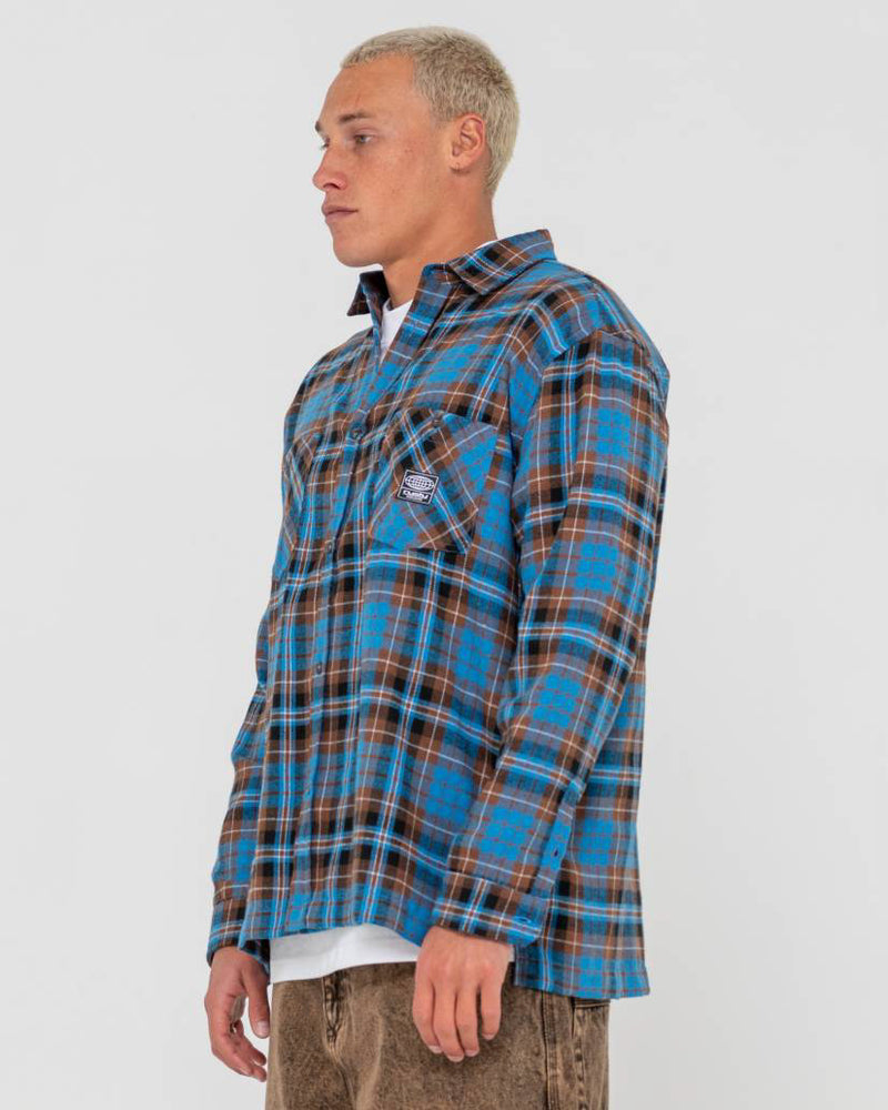 Side view of a man wearing a blue and brown plaid button-up flannel shirt with a relaxed fit and chest pockets.